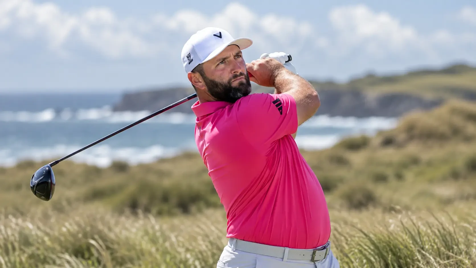 Jon Rahm hitting a tee shot on a links golf course