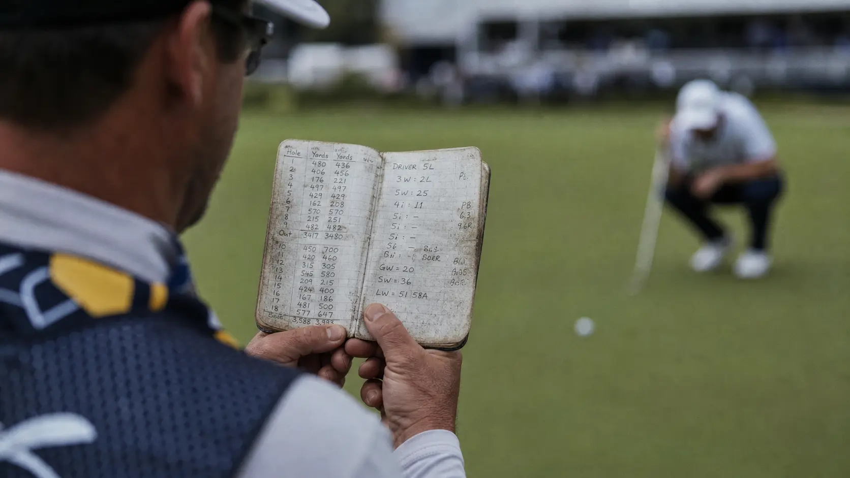 Golf caddie looking at strokes gained data in a yardage book