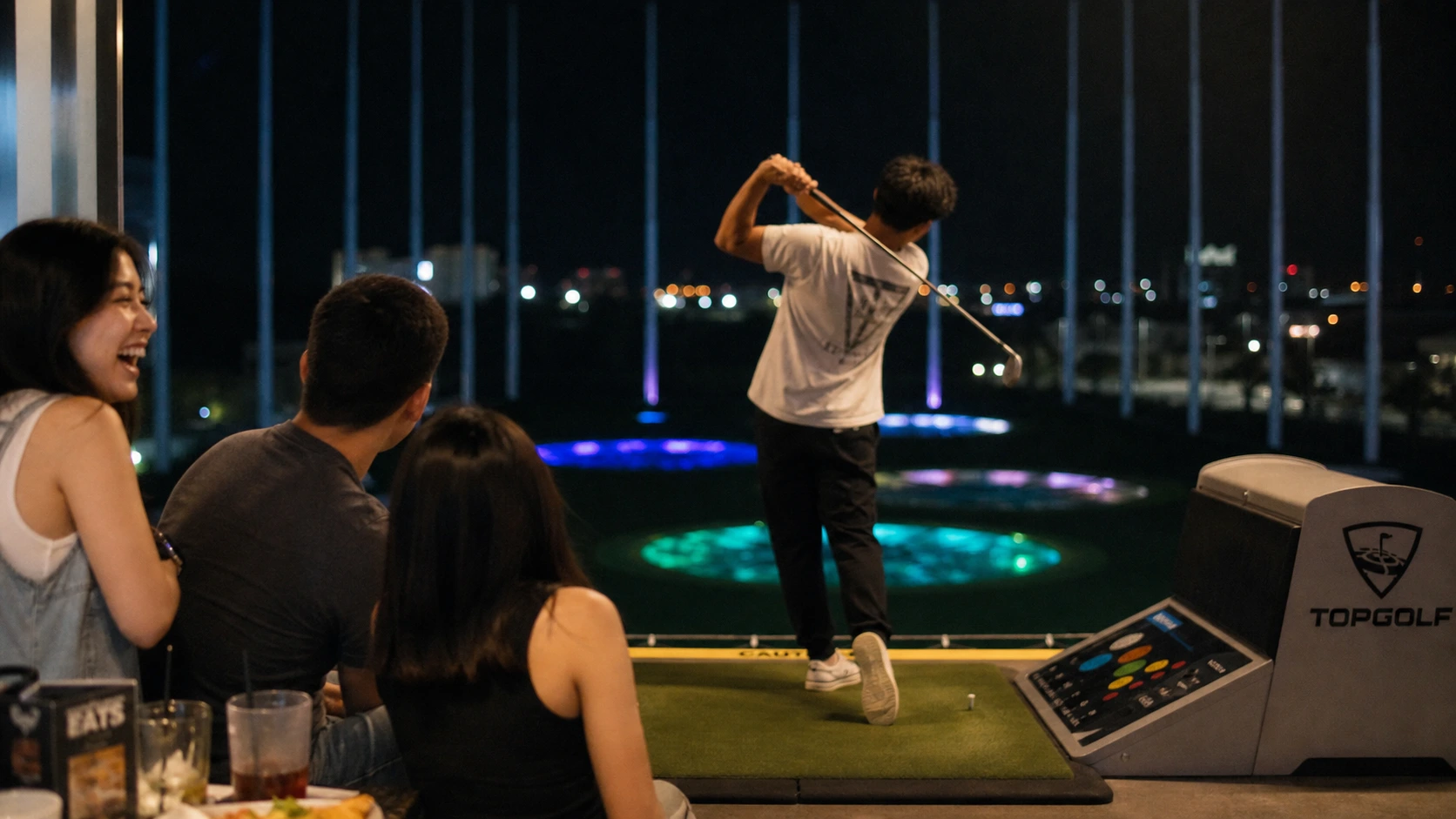 A relaxed group at a Topgolf bay dressed in casual jeans, t-shirts, and sneakers